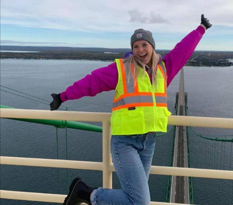 Girl in bright neon safety vest, hat, and gloves standing in front of a body of water